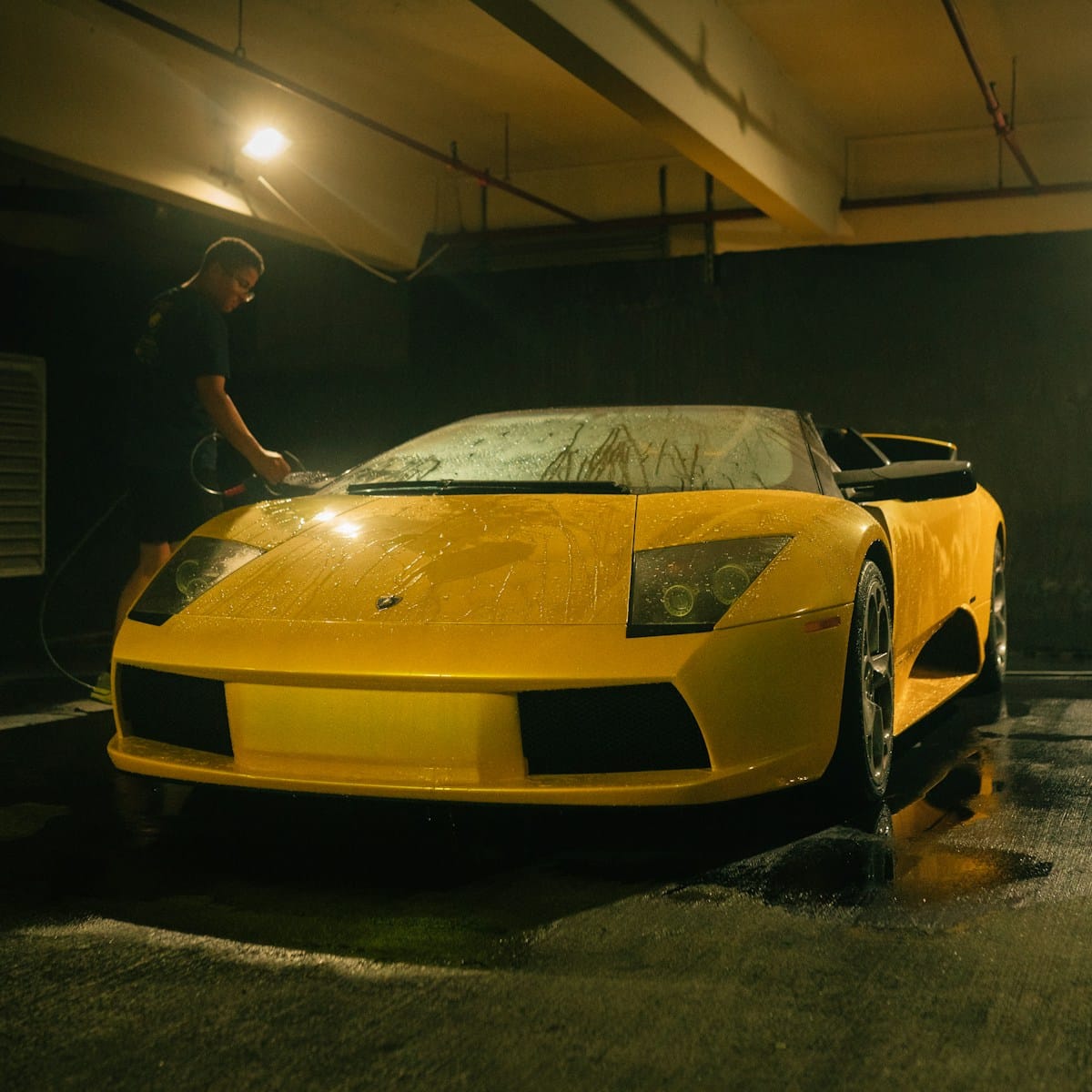 a man washing a yellow sports car in a parking garage